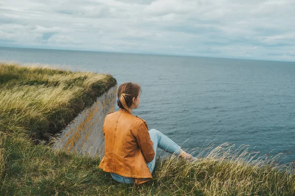 Una mujer de pie sobre hierba en el borde de la costa rocosa del mar Báltico. Vista trasera — Foto de Stock