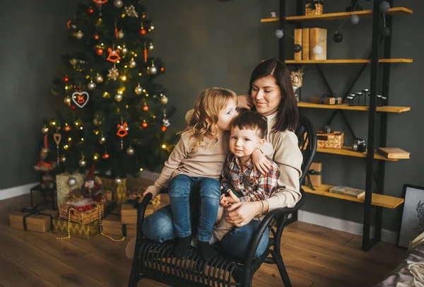 Mamá sentada en la silla entre sus hijos pequeños en su sala de estar en Navidad —  Fotos de Stock