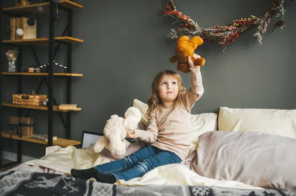 Niedliches kleines Mädchen, das mit Teddybär im Raum spielt, der für Neujahr dekoriert ist. Winterwochenenden. — Stockfoto