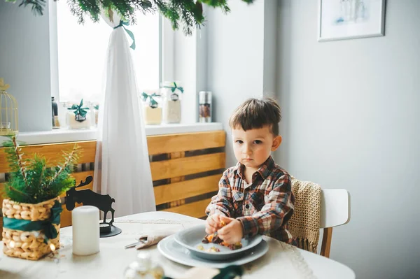 Kid sitting in kitchen near window with plate of tasty food. — Stock Photo, Image