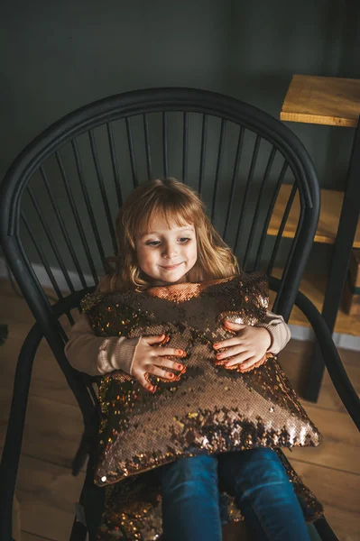 Kleine schöne Mädchen mit einem großen Kissen in den Händen sitzen auf schwarzem Holzstuhl — Stockfoto