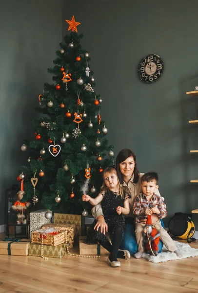 Feliz familia mamá y sus hijos en la noche de invierno en la sala de celebración con un árbol de Navidad y regalos . — Foto de Stock