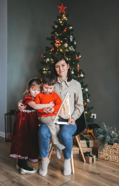 Familia feliz están sentados en la silla cerca del árbol de Navidad . — Foto de Stock