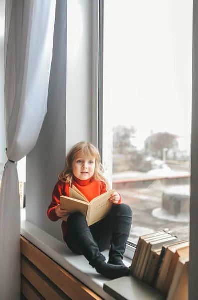 Menina com um livro no peitoril da janela — Fotografia de Stock