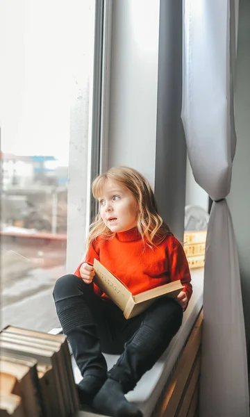 Sonhando menina lendo um livro no peitoril da janela no inverno em casa — Fotografia de Stock