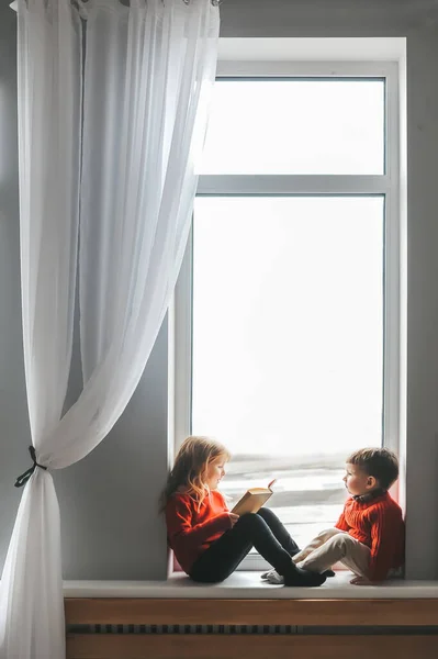 Linda niña leyendo libro para su hermano de dos años . — Foto de Stock