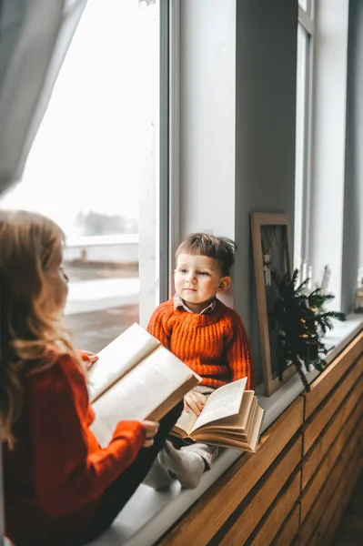 Hermano pequeño y hermana sentados en el alféizar de la ventana y leyendo libros . — Foto de Stock