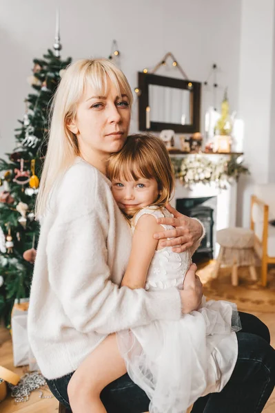 Feliz madre rubia y su hija pequeña abrazándose en casa . — Foto de Stock