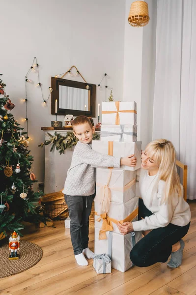 Feliz madre y su pequeño hijo. En frente de la familia, hay muchas cajas maravillosamente embaladas con regalos . — Foto de Stock