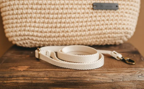 Trendy beige gebreide handtas en borstband op houten stoel. Handgemaakt patroon. — Stockfoto