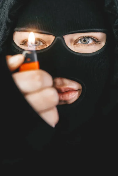 Muszlim nő terrorista tartja az öngyújtót az arca előtt, és a láng világítja meg az arcát.. — Stock Fotó