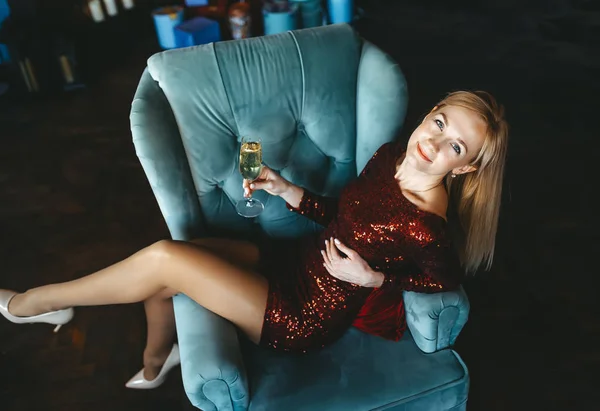 Jovem sorrindo bela mulher loira em vestido vermelho em uma poltrona com uma taça de champanhe. Vista superior — Fotografia de Stock