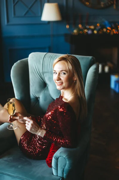 Молодая улыбающаяся красивая блондинка в красном платье в кресле с бокалом шампанского . — стоковое фото