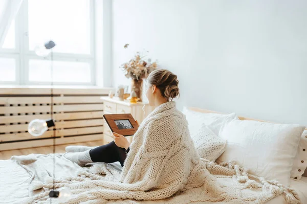 Joven mujer serena sentada en la cama en casa y sosteniendo un marco de imagen y viendo la imagen — Foto de Stock