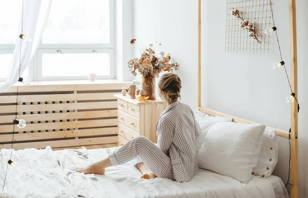 Rano piękna młoda kobieta siedzi na łóżku w przytulnym wnętrzu domu — Zdjęcie stockowe