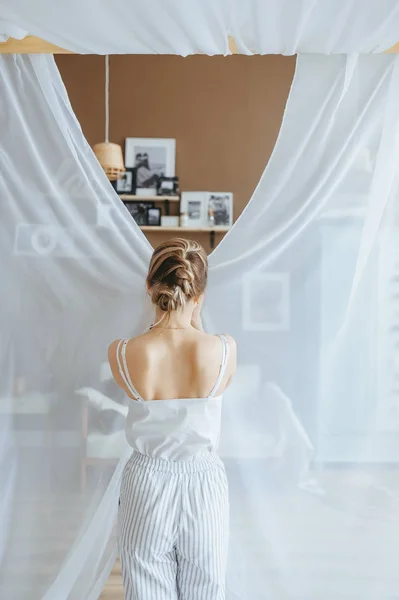 Жінка в піжамі, прокидається і стоїть біля штор у вітальні . — стокове фото
