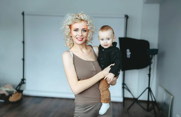 Blonde mom with make-up and little son poses in studio. — Stock Photo, Image