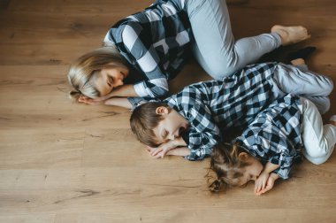 Anne ve iki çocuğu ahşap zeminde gözleri kapalı rahatça dinleniyorlar. Genel Görünüm