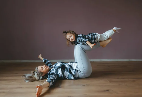 Mutter und Tochter machen Yoga-Übungen. kleines Mädchen balanciert auf Beinen der Mutter. — Stockfoto