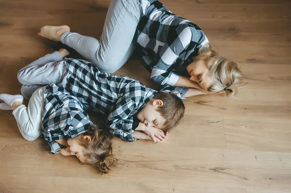 Draufsicht auf Mutter und ihre beiden Kinder in identischer Kleidung, die mit geschlossenen Augen auf dem Boden liegen. Ansicht von oben — Stockfoto