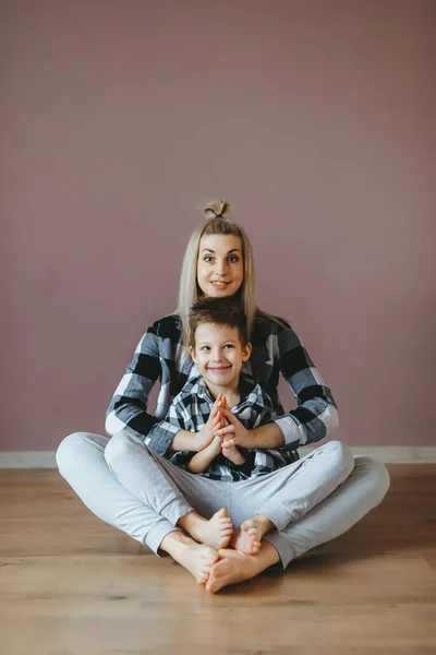 Junge Frau sitzt mit ihrem Sohn in Lotus-Pose auf dem Boden in einem Wohnzimmer. — Stockfoto