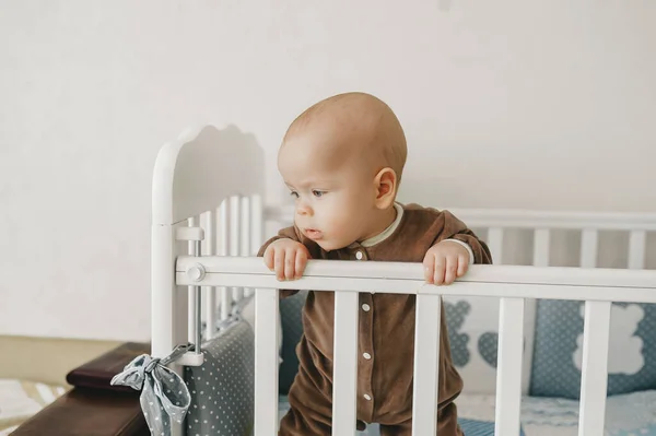 Infant child baby boy in wooden bed looking down indoors — Stock Photo, Image