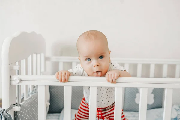 Cheerful baby boy sticking tongue out mouth and standing in the crib at home — Stock Photo, Image