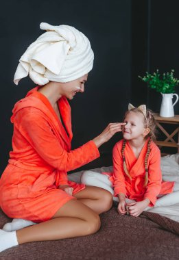Işıl ışıl anne, küçük kızıyla ve cildiyle ilgilenerek geçirdiği zamanın tadını çıkarırken yatakta oturuyor. Neşeli an.