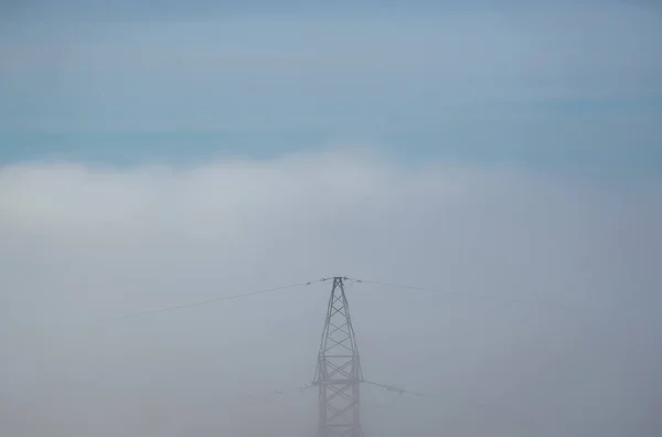 Power line hidden in thick fog in distance.
