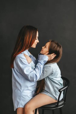 Siyah arka planda mavi gömlekli anne ve küçük kız. Yan görüş. Aşk ve Şefkat Konsepti