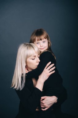 Koyu mavi arka planda gülücükler saçan, yanak yanağa kaynaşan güzel ve çekici anne ve kız. Sarılmak, kameraya bakmak. Anneler Günü. Dikey portre 