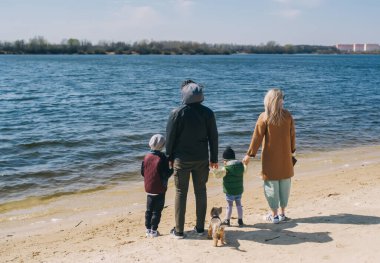 Aile nehir kıyısında duruyor ve uzaklara bakıyor. Mutlu aile doğada rahatlar. Arka plan