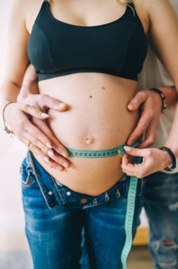 Göbek ölçen güzel hamile bir çift. Güzel hamile bir kadının çıplak karnına dokunurken bir erkeğin onu ölçtüğü görüntüler. Dikey görünüm