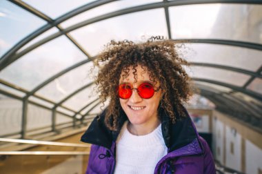 Şehir merdivenlerinde poz veren şık kırmızı gözlüklü kıvırcık genç hippi kız. Yakın plan portre