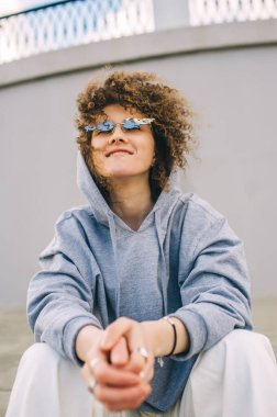 Şehir merdivenlerinde oturan şık gözlüklü kıvırcık ergen hippi kız. Yakından bir portre. Alt görünüm