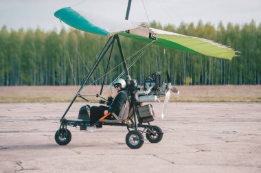 Pilot akıllı bir telefon kullanıyor ve kalkış pistinde moto askılı planörle selfie çekerken gülümsüyor.