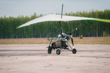 Moto askılı planör, bulutlu mavi gökyüzünün arka planına karşı çimen pistinden kalkıyor. Arka görünüm