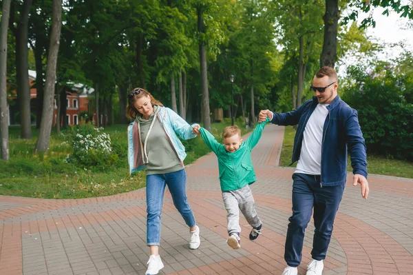 家族は街の公園の外を歩いている 家族は手をつないでいる 息子は父と母の間にいる — ストック写真