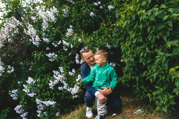 Dad hugs little son and laughs in a flowering garden.