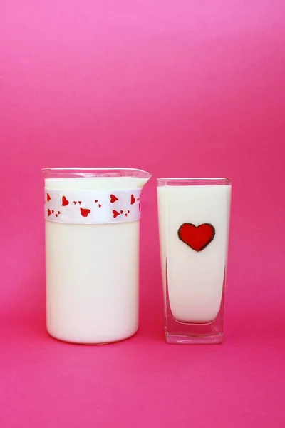Кувшин и стакан молока на розовом фоне, концепция молока — стоковое фото