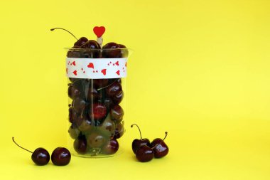 Sarı bir arka plan üzerinde izole bir cam sürahi taze kiraz meyveleri