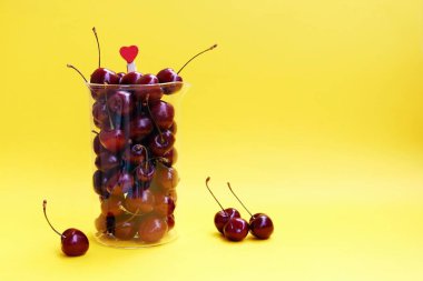 Sarı bir arka plan üzerinde izole bir cam sürahi taze kiraz meyveleri