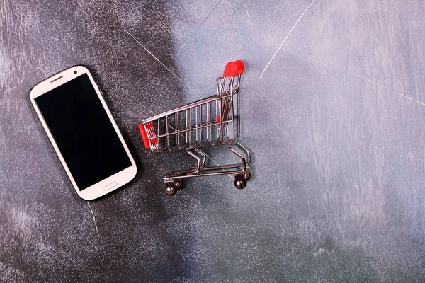 Online shopping concept, shopping cart and smart phone on textured background