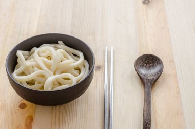 Ahşap arka planda siyah kasede beyaz udon eriştesi.