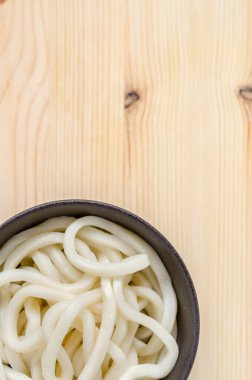 Ahşap arka planda siyah kasede beyaz udon eriştesi.