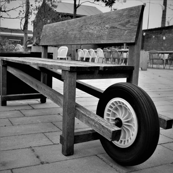 Black and white picture with weathered wooden wheelbarrow bench in industrial area