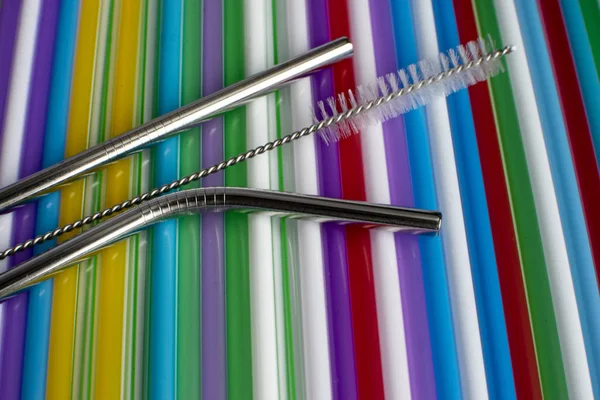 Reusable metal straws with a portable case - stainless steel, an environmentally friendly set of drinking straws with cleaning brushes. Against the background of plastic tubes for a cocktail.