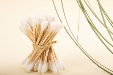 Pastel arka planda bambu pamuk tomurcukları. Yeşil çimen yaprakları bileşimi canlandırır. Kulak için biyo-çözünebilir pamuk tomurcukları