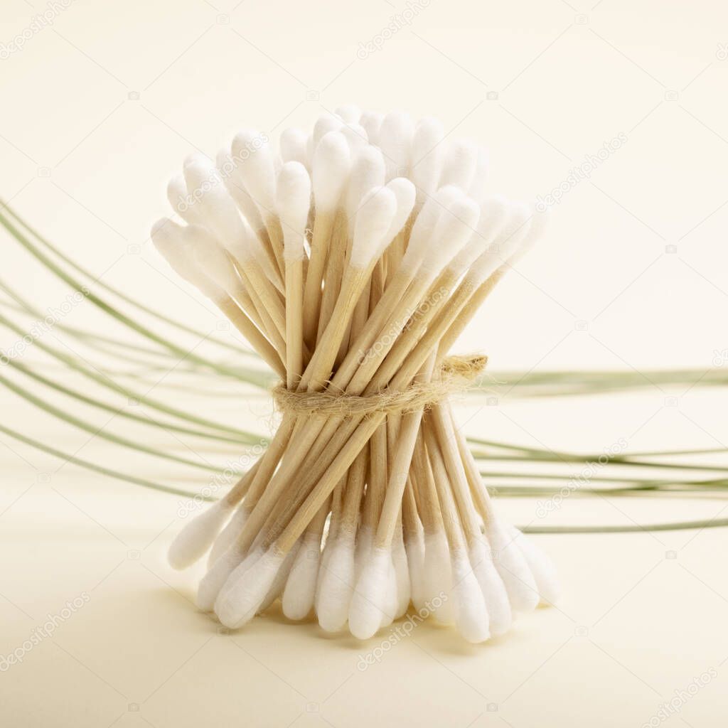 Set of bamboo cotton buds on a pastel background. Green leaves of grass revitalize the composition.Biodegradable Cotton Buds for Ear