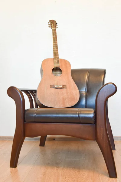 Acoustic six-string guitar and vintage leather armchair in the i